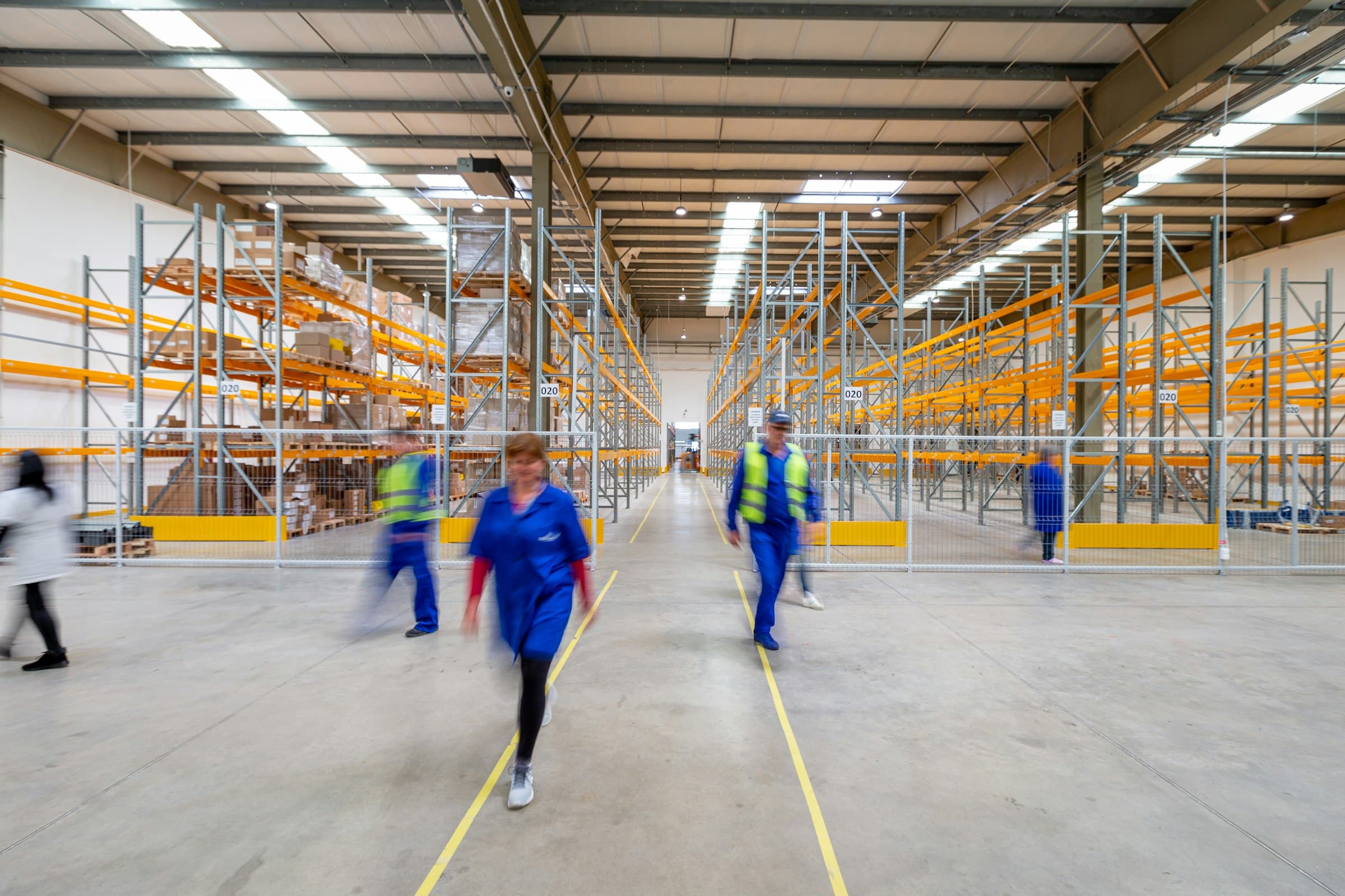 Fulfillment-Halle mit Warenregalen, Mitarbeitende in Bewegung